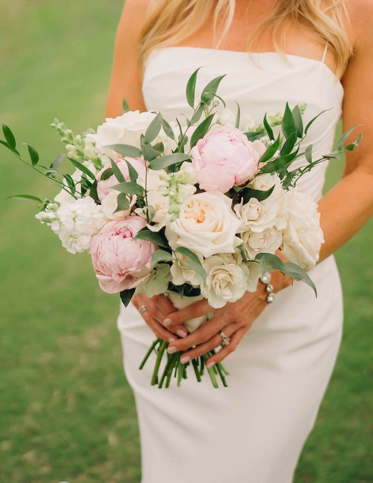 Wedding bouquet of pink peonies and cream garden roses held by a bride