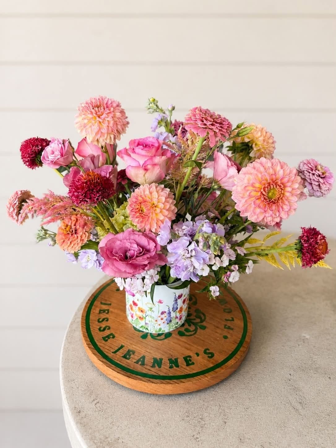 Pink and coral dahlias in a floral ceramic pot on a Jesse Jeanne's serving board