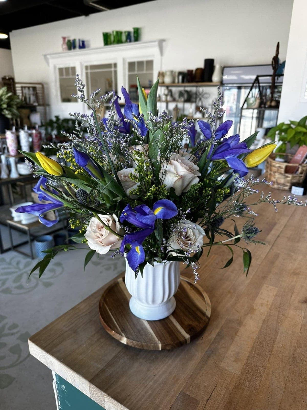 Fresh flower arrangement of blue iris, yellow tulips, and cream roses in a white fluted vase