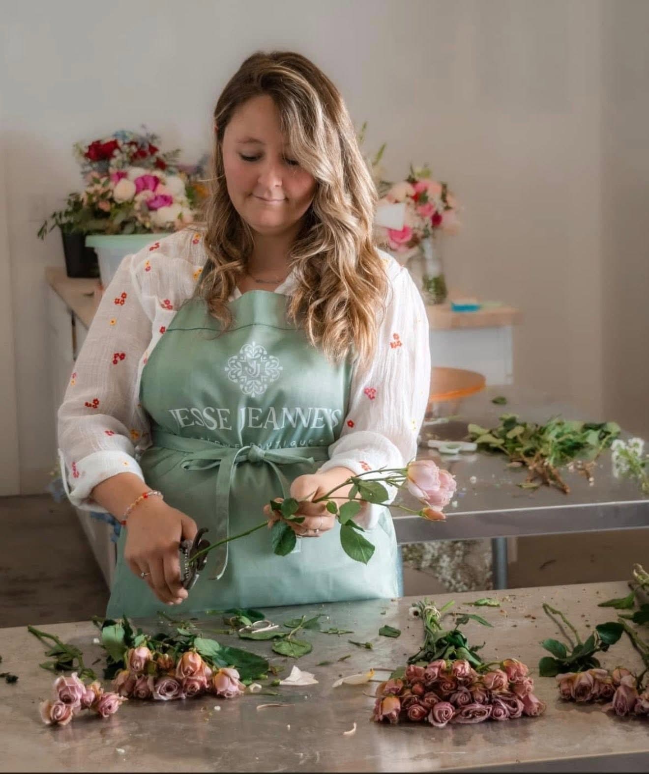 Jesse in a Jesse Jeanne's apron trimming roses at the design table