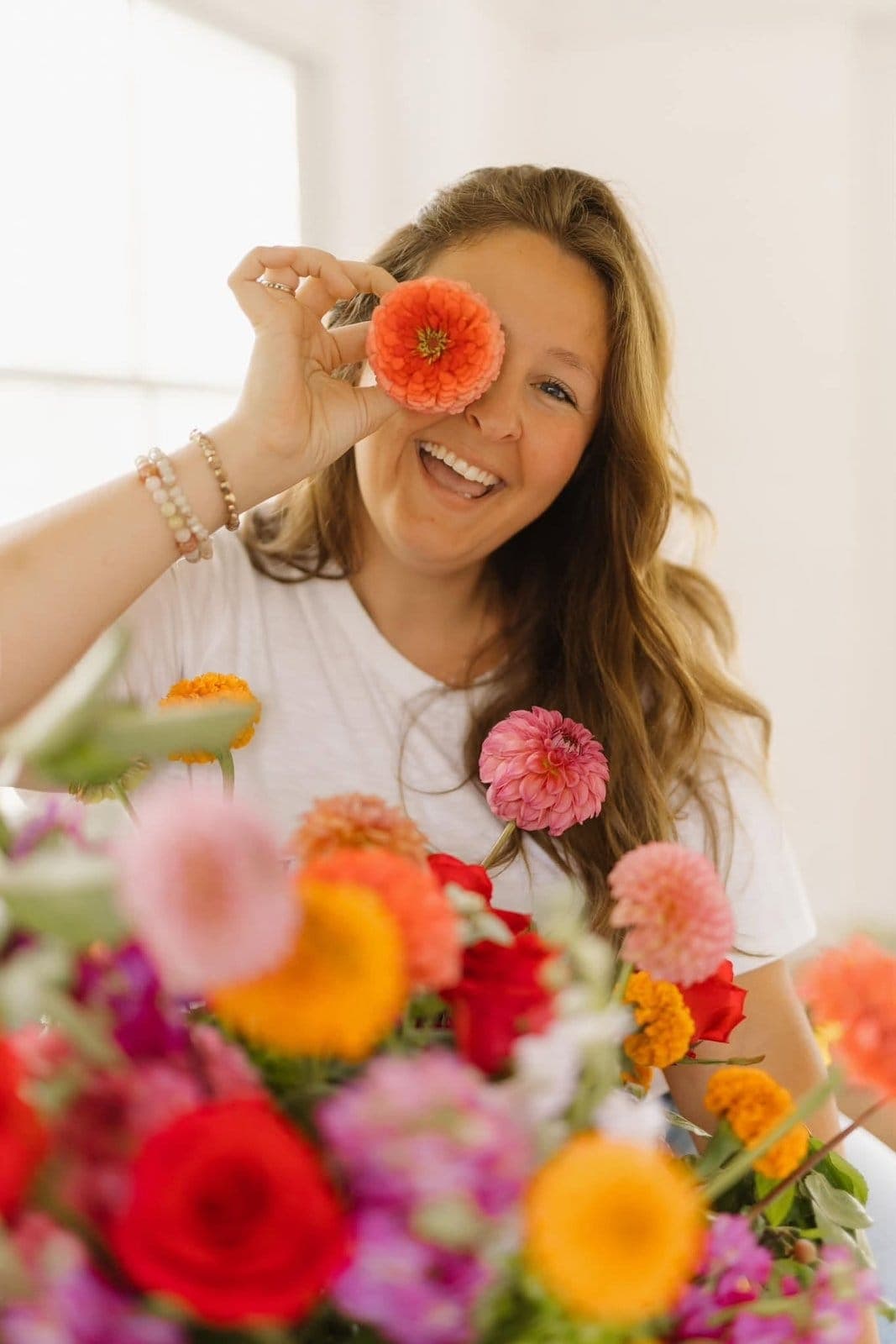 Jesse Diekhoff laughing while holding a coral zinnia up to her eye