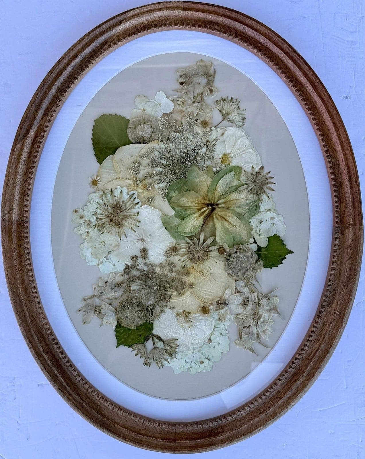 Preserved white bridal bouquet pressed into an oval wood frame, dried to cream and green