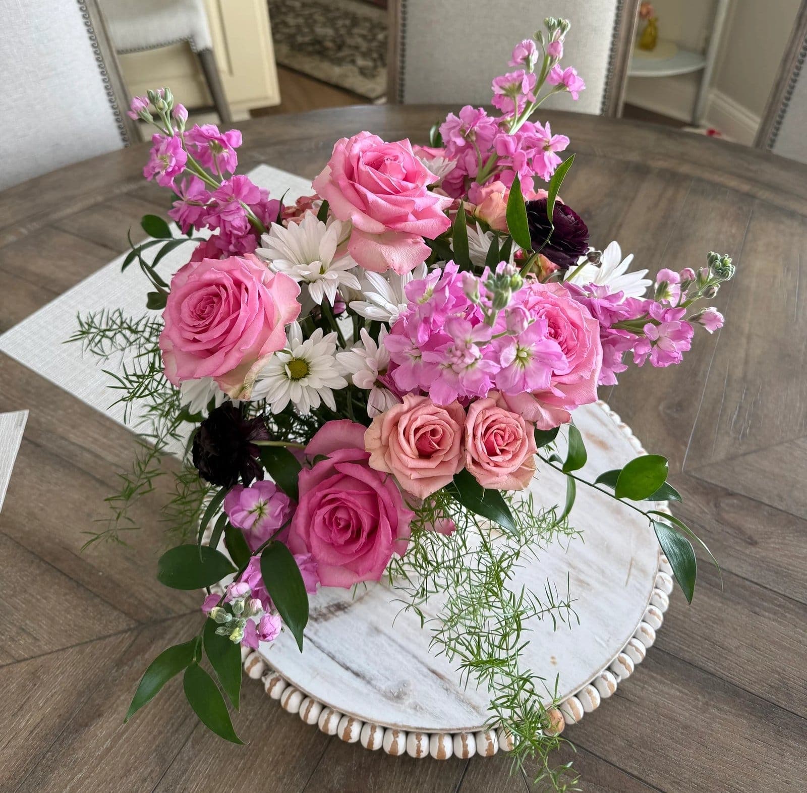 Pink roses, stock, and white daisies arranged on a beaded tray at home