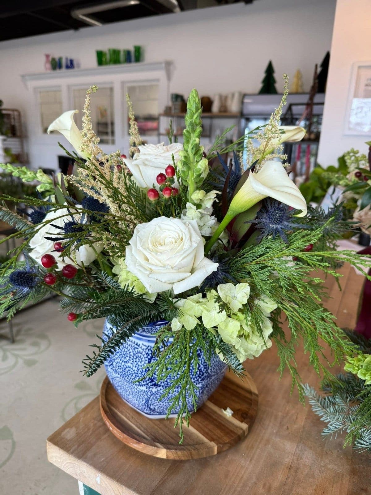 Winter arrangement of white roses, calla lilies, and evergreen in a blue and white pot
