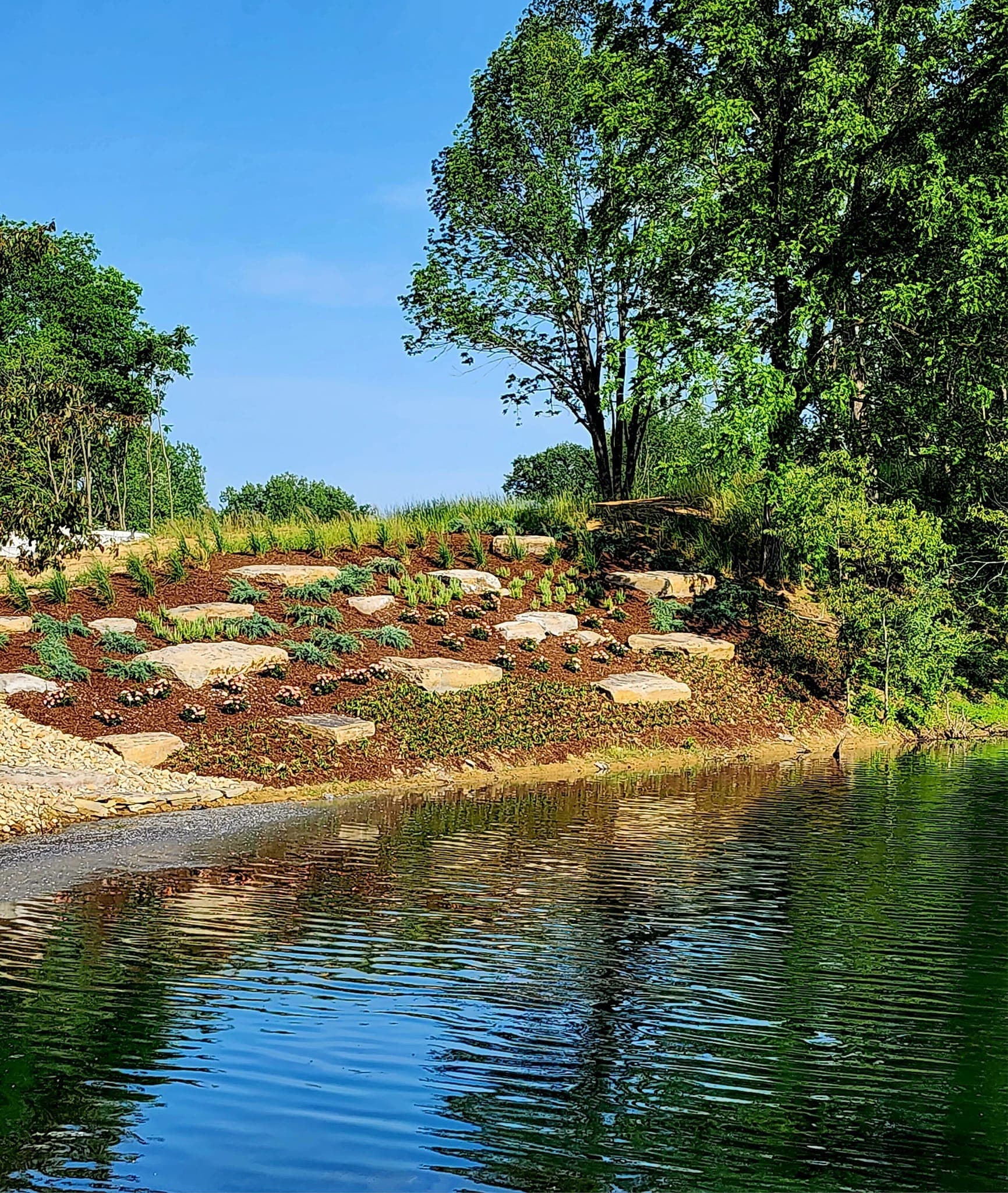 Lakeside landscape with mature plantings, stone features, and waterfront views