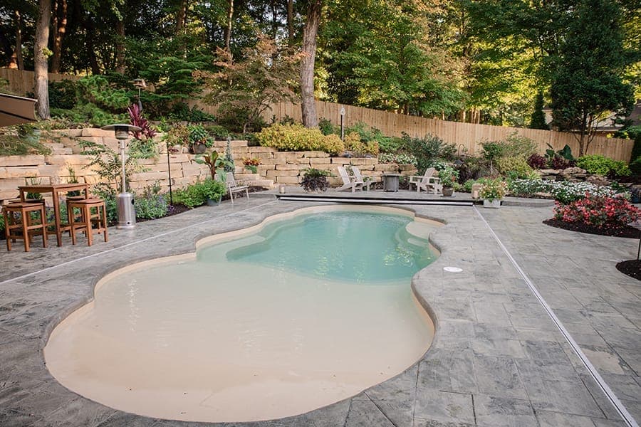 Fiberglass pool with paver patio, retaining wall, and landscape plantings